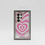 A pink and white heart-patterned protective phone case in its black retail packaging, displayed on a white table inside a store.