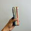A hand holds a stack of three slim, textured phone cases in navy blue, gold, and coral orange, shown from the side against a blurred indoor background.