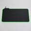 A large black gaming mouse pad with a glowing green LED border, shown against a solid black background. A small brand tag is visible in the top-left corner of the pad.