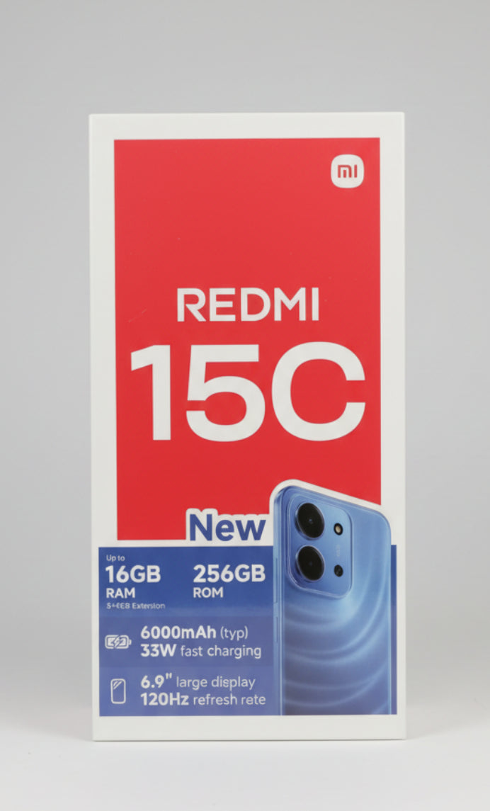 Redmi 15C smartphone retail packaging card held in a hand, showing a pink front panel with large white 'REDMI 15C' text, a blue phone illustration, and feature callouts including 16GB RAM, 256GB ROM, 6000mAh battery, and 6.9" display. Main image