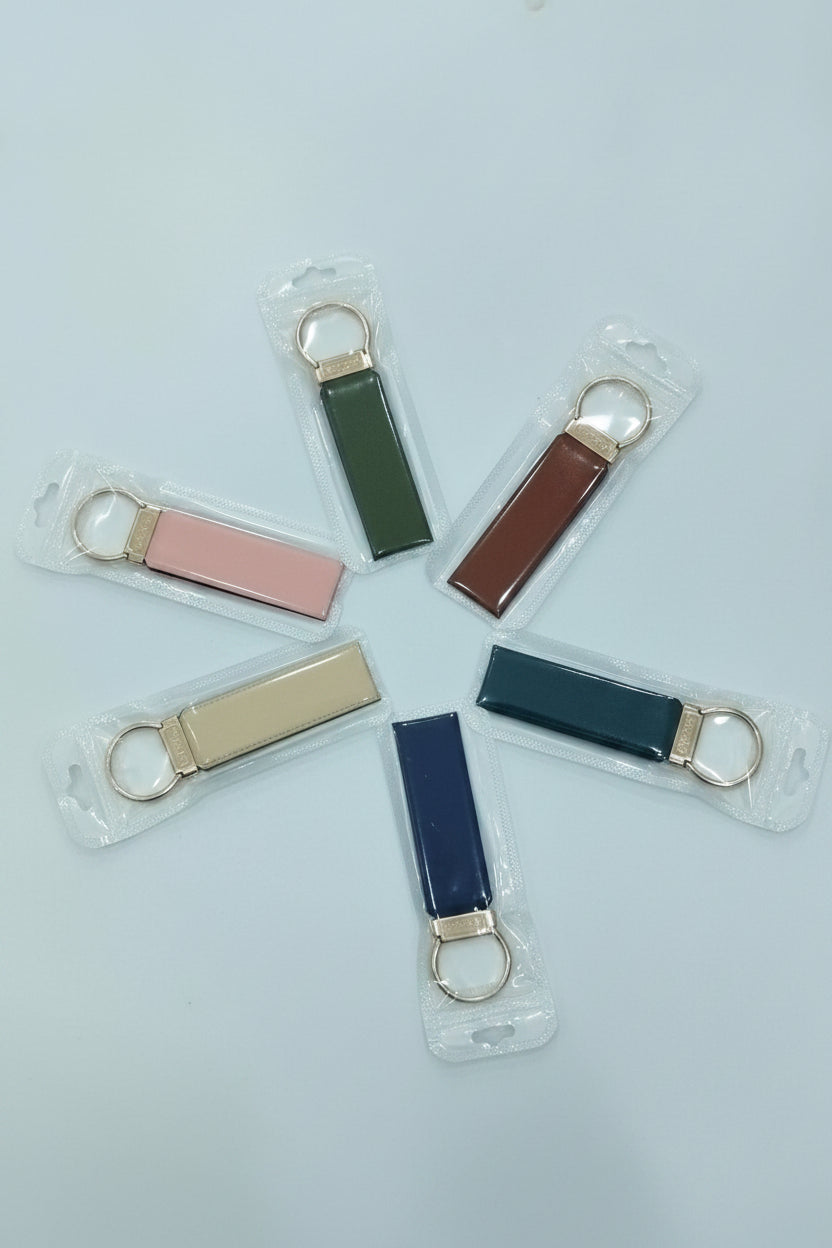 Six small rectangular keychain fobs in assorted colors, each in clear plastic packaging with a gold-tone key ring, arranged in a circle on a light background.