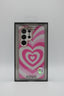 A pink and white heart-patterned phone case in its original retail packaging, featuring a glittery finish and a clear camera cutout.