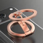 Rose gold metal phone stand with a built-in kickstand feature, shown attached to a smartphone on a dark reflective surface.