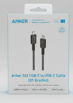 A hand holding a boxed Anker 322 USB-C to USB-C cable in a retail store setting. The white box shows the Anker brand name, product details, and compatibility text, with other packaged goods blurred in the background.