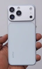 A hand holding a white ATELY smartphone, showing its back panel with a large triple-camera cutout and a matte finish, set against a blurred background.