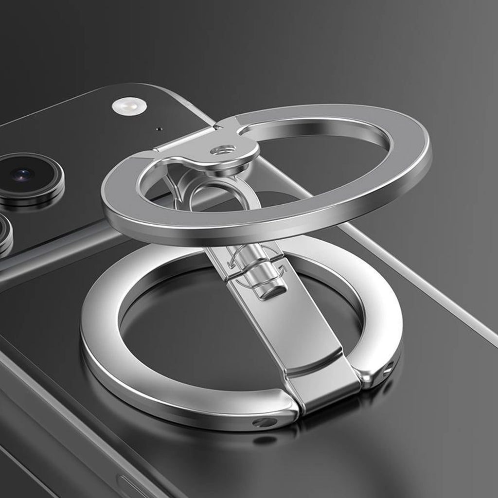 A metallic silver phone grip ring with a built-in kickstand, shown attached to the back of a black smartphone on a dark reflective surface.